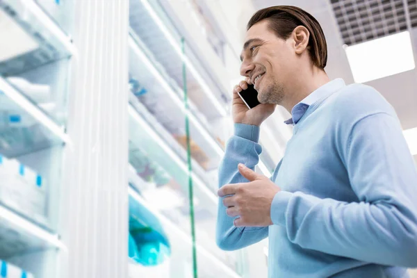Lächelnder Mann, der in einer Apotheke steht und mit einem Smartphone spricht — Stockfoto