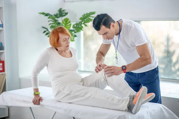 Ernstige jongeman kijkt naar zijn patiënten knie — Stockfoto