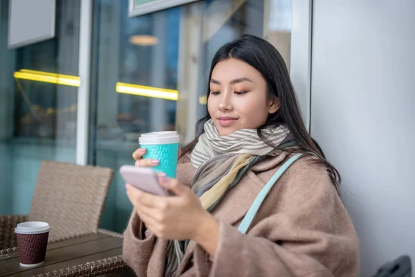 Bastante asiático joven mujer tomando café fuera y mensajes de texto —  Fotos de Stock