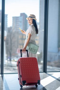 Pencerenin yanında duran siyah saçlı, şapkalı genç kadın.