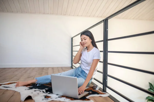 Egy fiatal nő ül a földön laptoppal, gépel, sínekre támaszkodik, egyik kezét az állára teszi — Stock Fotó