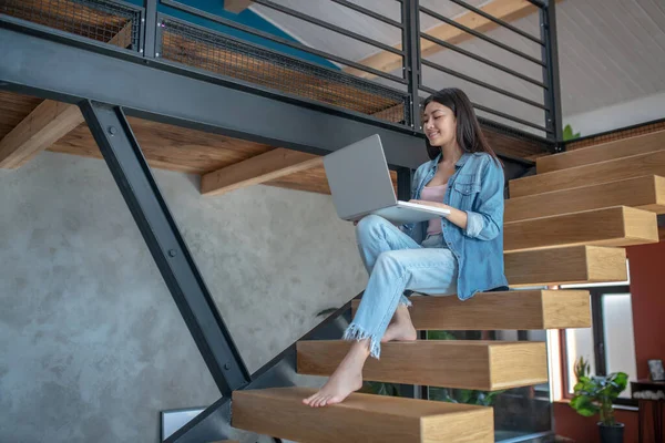 Fiatal nő ül a lépcsőn, kezében laptop térden, gépelés — Stock Fotó