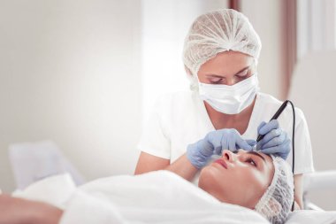 Kozmetik uzmanı eldiven takıyor. Kadın alnını temizliyor.