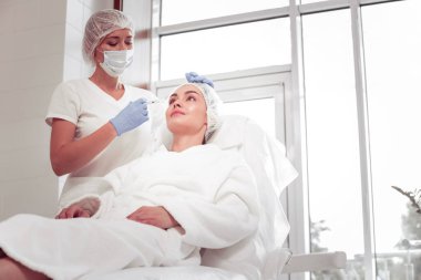 Kozmetik uzmanı, müşteri için güzellik fotoğrafları çekerken pencerenin yanında duruyor.