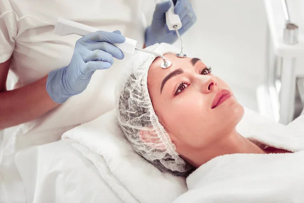 Experto en belleza que usa guantes azules para limpiar la cara de la mujer de ojos oscuros — Foto de Stock