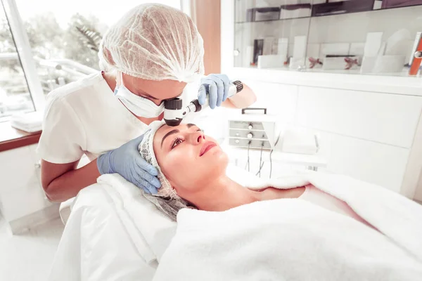 Cosmetoloog draagt handschoenen zorgvuldig reinigen huid van de klant — Stockfoto