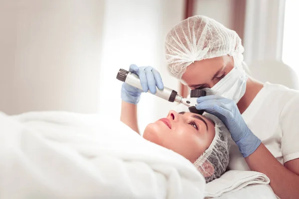 Dermatologo indossando maschera e guanti esaminando la pelle del cliente — Foto Stock