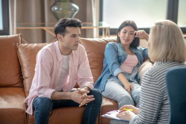 Koyu saçlı, uzun boylu bir adam kız arkadaşının yanında oturuyor ve psikoloğu dinliyor.