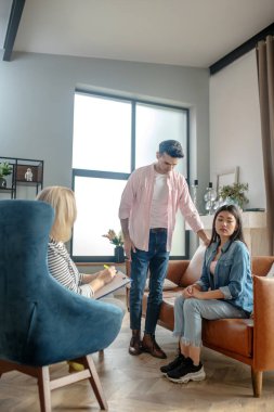 Koyu saçlı, uzun boylu bir adam kız arkadaşının yanında duruyor.