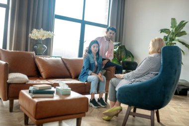 Koyu saçlı uzun adam ve kız arkadaşı kanepede oturup psikologla konuşuyorlar.