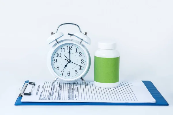 Белый будильник и бутылка таблеток на столе с картой пациента — стоковое фото