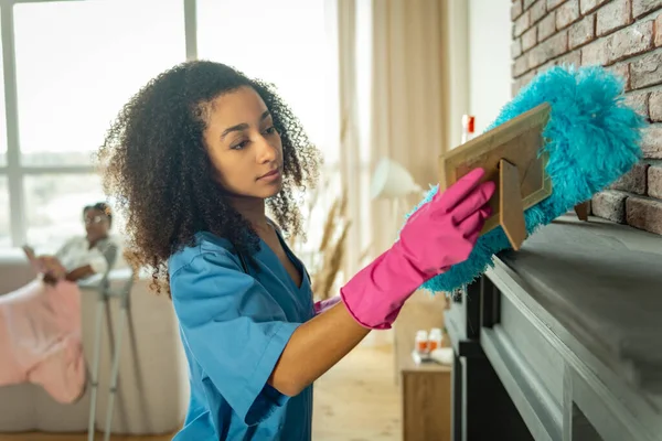 Sorgfältige junge Krankenschwester reinigt die Wohnung vom Staub — Stockfoto