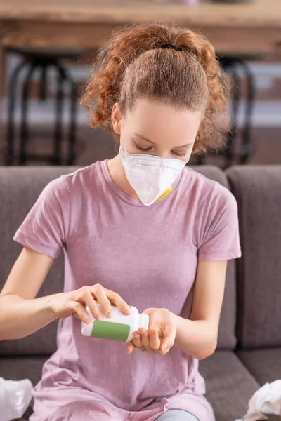 Chica en una máscara respiratoria conseguir pastillas de la botella — Foto de Stock