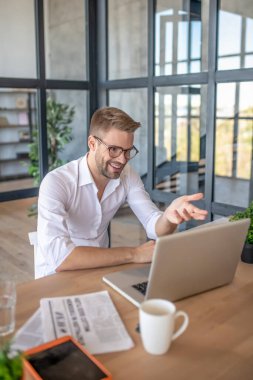 Beyaz gömlekli genç adam internette konuşuyor.