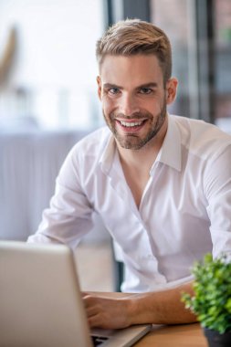 Beyaz gömlekli genç adam güzelce gülümsüyor.