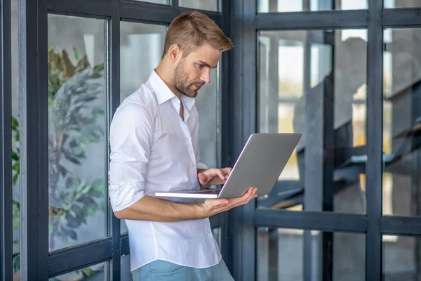 Joven hombre guapo sosteniendo su portátil mientras trabaja desde casa — Foto de Stock