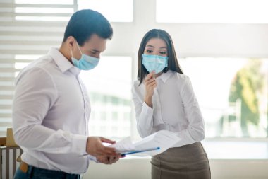 Koruyucu maskeli meslektaşlar ofiste birlikte çalışıyorlar.