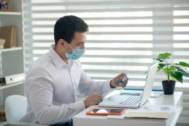 Beyaz gömlekli bir adam laptopunu dezenfekte ediyor ve olaya dahil gibi görünüyor.