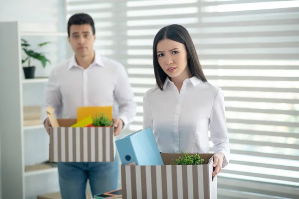 Расстроенные молодые коллеги-мужчины и женщины, держащие коробки со своими личными вещами — стоковое фото