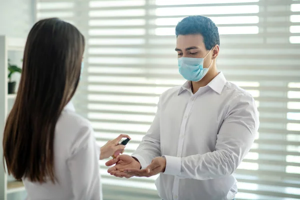 Long-haired girl spraying sanitizer on her colleagues hands — Stock Photo, Image