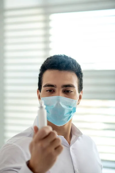 Hombre de pelo oscuro con una máscara protectora sosteniendo un spray desinfectante en su mano — Foto de Stock