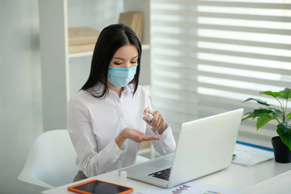 Dunkelhaarige Frau mit Gesichtsmaske sprüht Desinfektionsmittel auf ihre Hände — Stockfoto