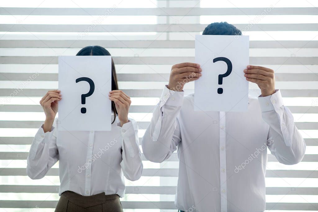 Male and female colleagues standing at the window, covering thier faces with papers with question marks