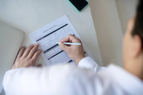 Mörkhårig man i vit skjorta signerar arbetslöshetsansökan — Stockfoto