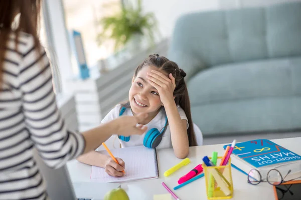 Liten leende flicka skolflicka vid bordet med läroböcker. — Stockfoto