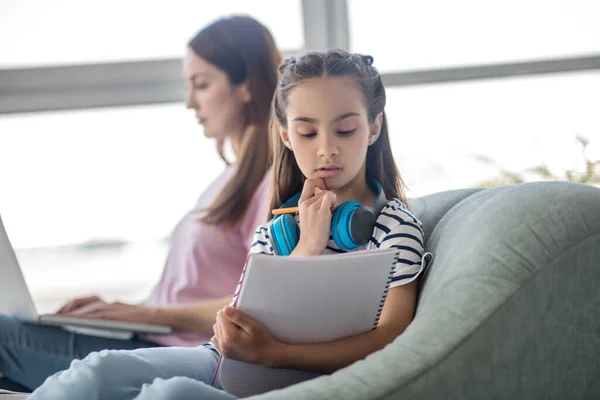 Dziewczyna ze słuchawkami i notatnikiem, mama z laptopem. — Zdjęcie stockowe