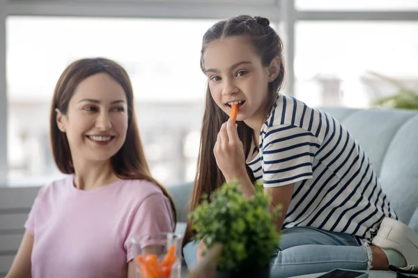 Mamá mirando a su hija comiendo una zanahoria . — Foto de Stock