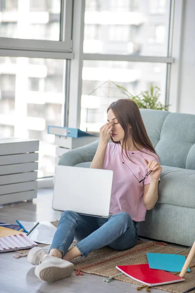 Jonge vrouw neemt af bril zitten op de vloer. — Stockfoto