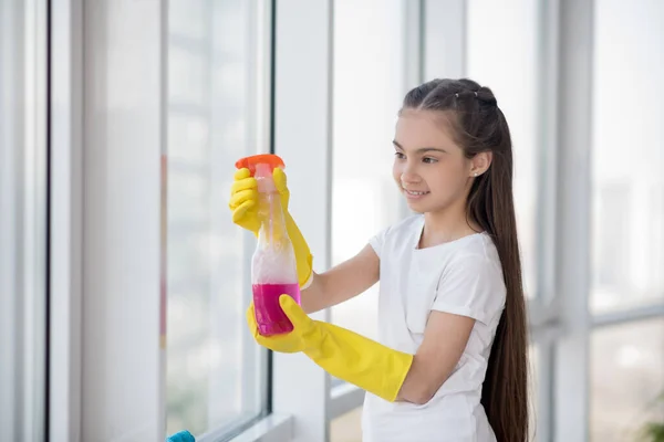 Lang haar tiener meisje in rudimenten wassen van een raam. — Stockfoto
