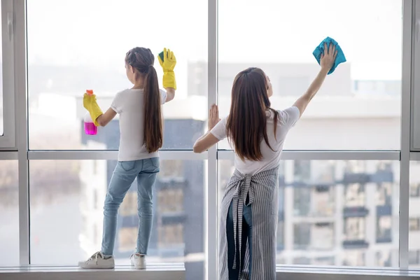 Ibu dengan anak perempuan mencuci jendela besar di rumah. — Stok Foto