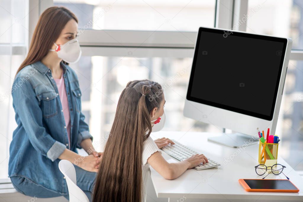 Woman and girl in front of computer in protective masks.