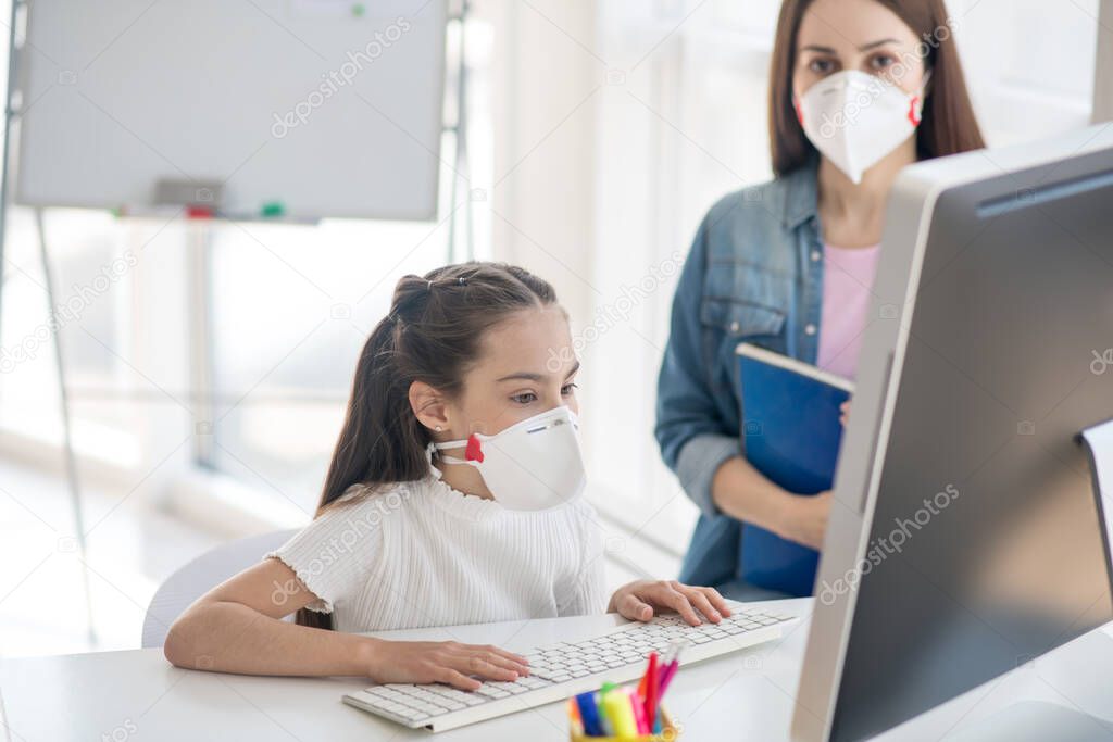 Girl and woman in protective masks looking at the computer.