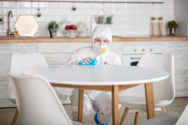 Beyaz iş elbiseli ve koruyucu eldivenli kadın mutfakta dezenfeksiyon yapıyor.