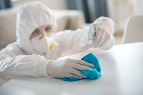 Жінка в білому робочому одязі і захисних рукавичках приправляє антисептичну рідину на столі — стокове фото