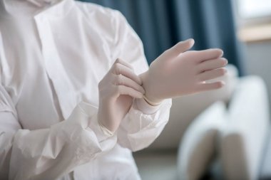 Beyaz iş elbiseli kişi dezenfeksiyon öncesi koruyucu eldiven giyiyor
