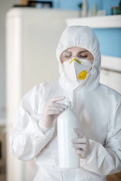 Mulher de fato de trabalho branco e luvas abrindo uma garrafa com líquido anti-séptico — Fotografia de Stock