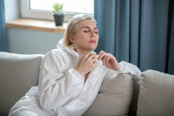 Blonde Frau in weißer Arbeitskleidung sitzt auf dem Sofa — Stockfoto