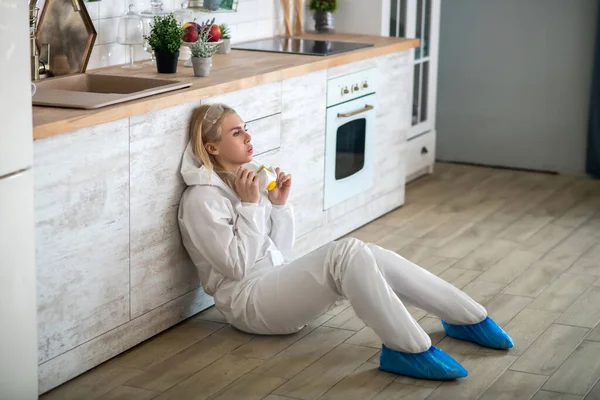 Beyaz iş elbiseli sarışın kadın mutfakta yerde oturuyor ve yorgun hissediyor. — Stok fotoğraf