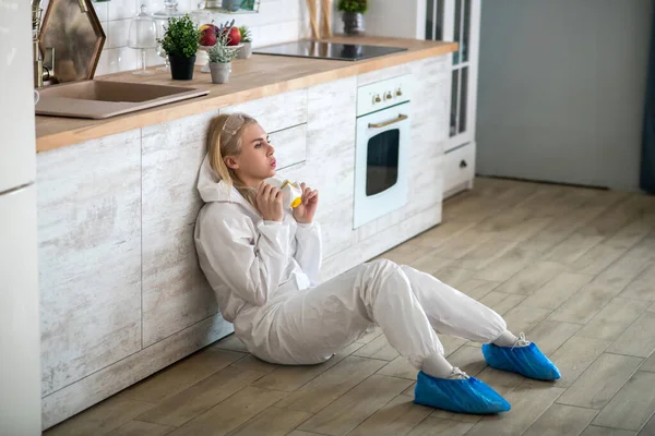Blondine vrouw in witte werkkleding zittend op de vloer in de keuken — Stockfoto