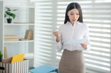 Genç esmer kadın elinde kağıt parçasıyla onu okuyor.