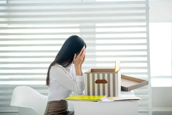 Jeune femme brune bouleversée assise à son bureau, fermant son visage avec les mains — Photo