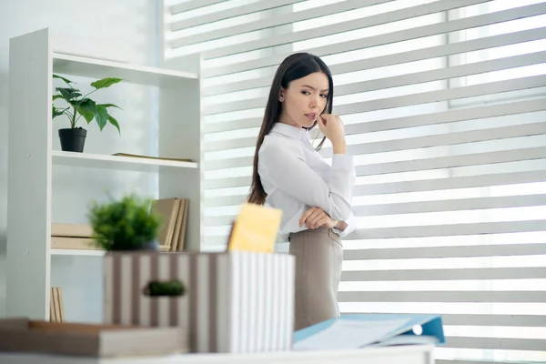 Jong brunette vrouw staan bij het raam, kijken naar haar doos met persoonlijke spullen, staan op het bureau — Stockfoto