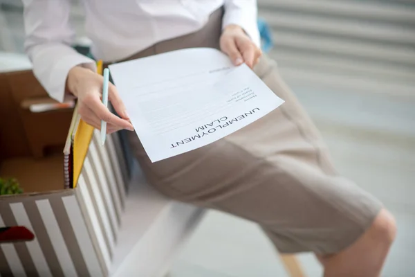 Молодая женщина заполняет заявление о безработице на коленях — стоковое фото