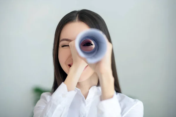 Mladá brunetka žena dívá přes papírové trubice, usmívá — Stock fotografie