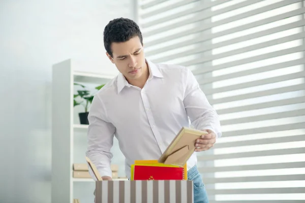 Brunette man staat aan zijn bureau, verzamelt zijn persoonlijke spullen in een doos — Stockfoto
