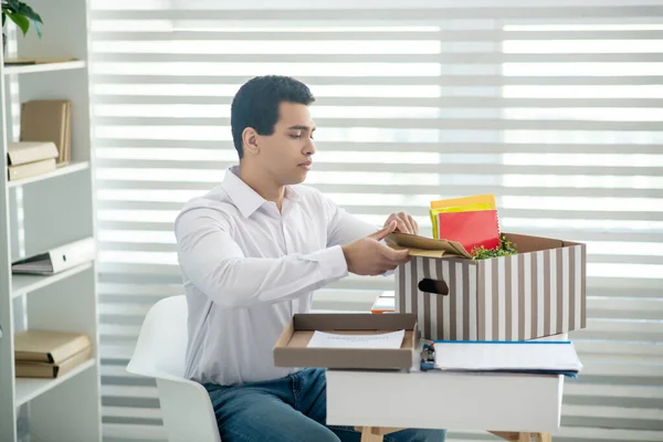 Morena macho sentado en su escritorio, poniendo sobres en la caja con sus cosas personales — Foto de Stock